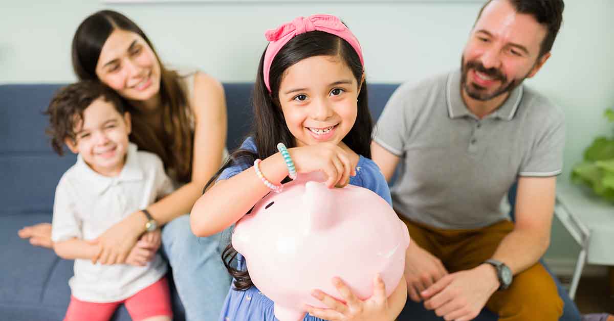 cute little girl putting money on a pink piggy bank to save for a new toy for her and her small brother