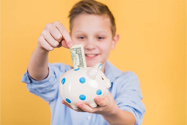 boy inserting currency note in the polka dot ceramic piggy bank 