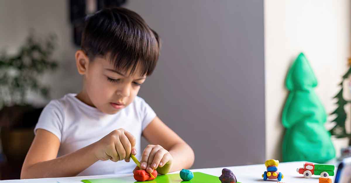 boy playing with colored plasticine and making figures on the white table