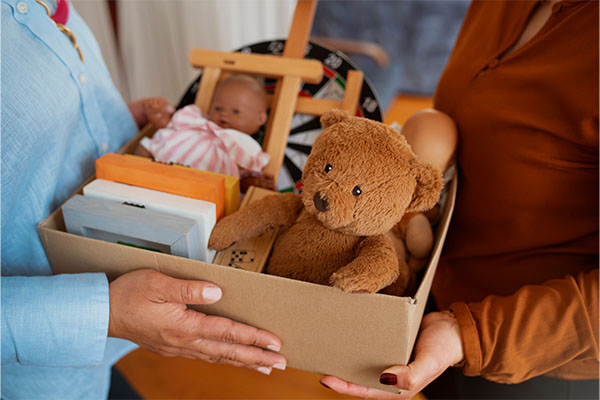 Two women, one handing a small item to the other, representing the act to donate old toys.
