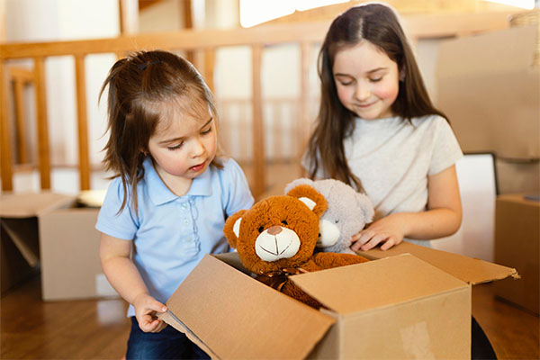 Two young girls happily playing with various toys on the floor, showcasing the joy and engagement toys bring