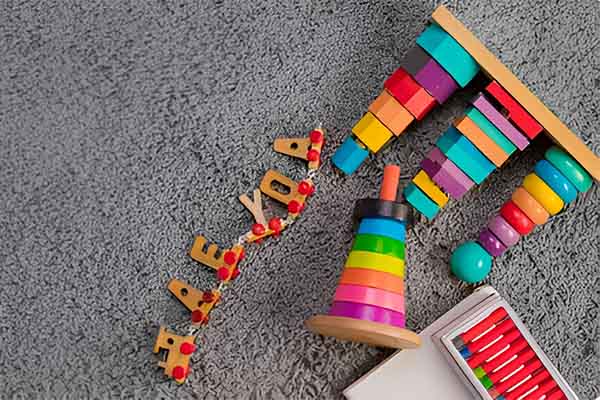 A variety of wooden educational toys arranged on a grey carpet, including a rainbow stacker, xylophone, and alphabet pieces