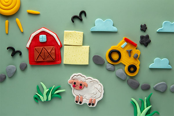 A playful farm scene made of colorful clay, featuring a red barn, tractor, sheep, grass, and clouds on a green background
