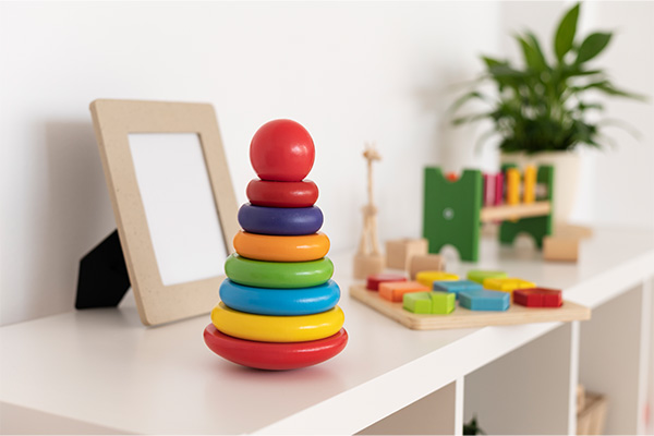 A colorful stacking ring toy placed on a white shelf next to a picture frame and other wooden toys.