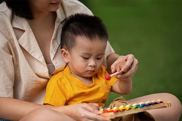 mother and kid sitting on grass mother teaching kid to play with musical toy