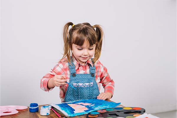 girl painting with gouache at wooden table